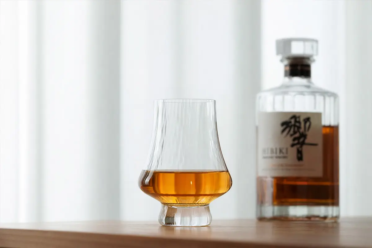 Glencairn-style whiskey tasting glass with amber whisky and bottle in soft background
