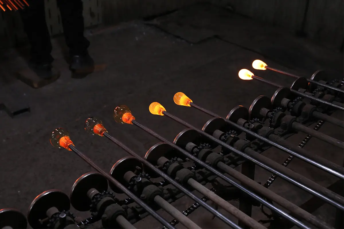 Workers gathering molten glass during the glass cup molding process