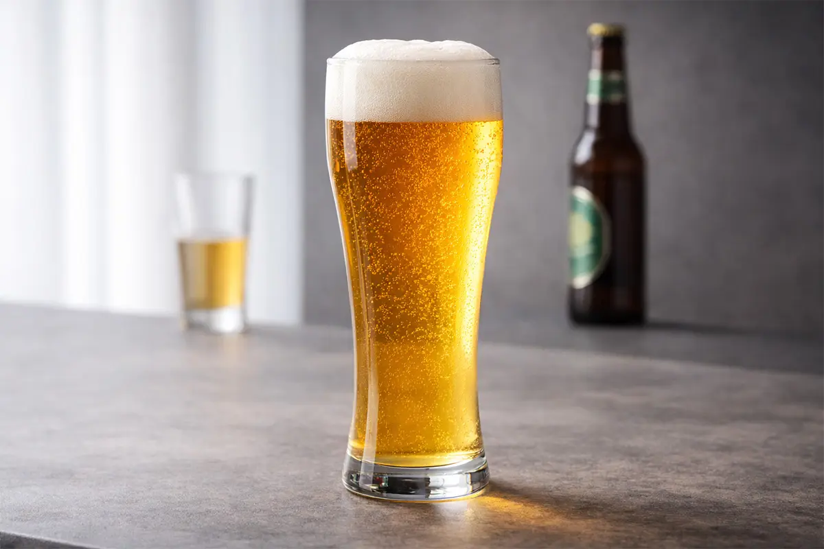 Tall pilsner beer glass with golden beer and foam head