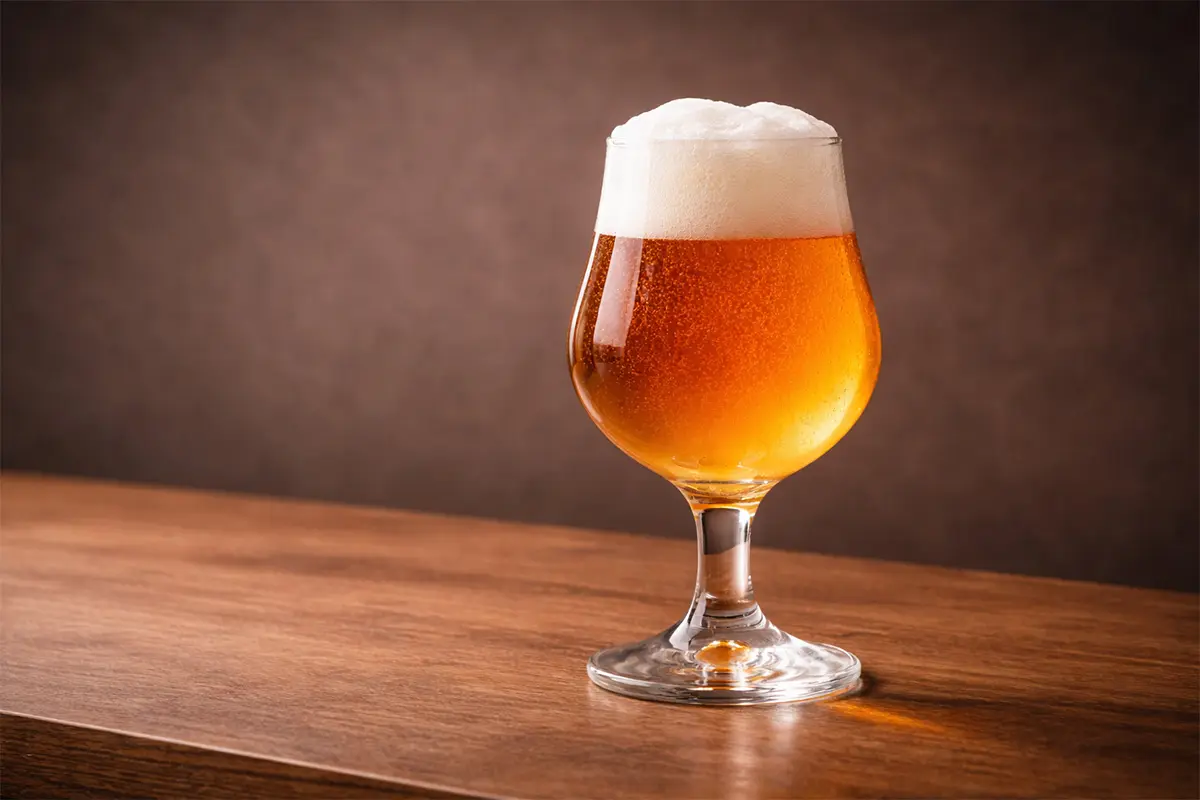 Tulip Belgian goblet beer glass with amber craft beer on wooden table